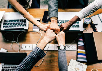 Coworkers in an office touching fists together. 5 Simple Office Cleanup Tips to Keep Staff & Employees Happy | The Budd Group