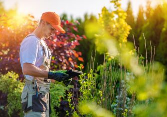 Landscaper looking at flowers in an industrial space What Industrial Landscaping Services Are Right for My Commercial Business This Summer?