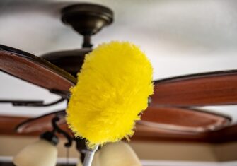 Person dusting a ceiling fan with a yellow duster Top 4 Reasons Spring Is the Best Time for High Dusting Your Office