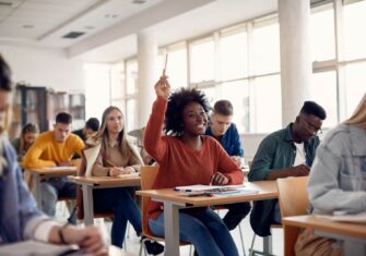 Girl raising her hand in a school classroom. How the BreatheWell Program Protects Students During Back-to-School Season