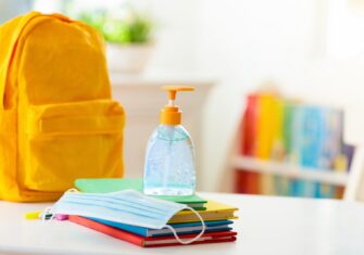 Hand sanitizer and a mask on top of school books. 5 Steps to Manage Sickness in Your K-12 School System