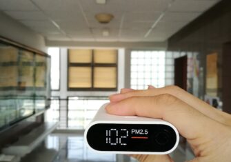 Hand holding up an alarm clock in a school hallway. Ensure Optimal Air Quality with Changing Seasons at Your School